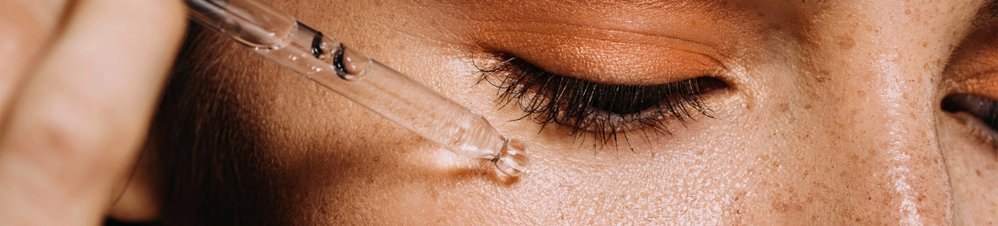 woman holding skin care dropper to under eye and applying serum